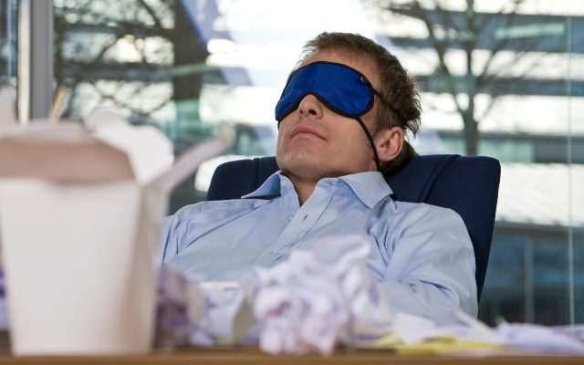 businessman taking a nap at his desk wearing a sleep mask